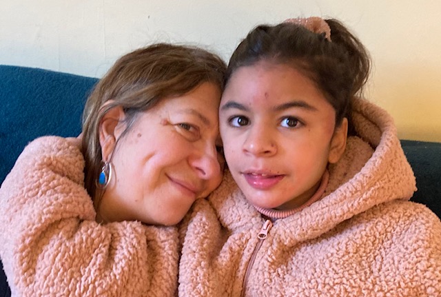 A mum and daughter hugging on the sofa, smiling warmly.