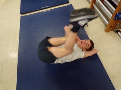 A young man rolling onto his back in PE